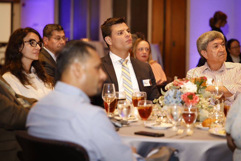Attendees seated at a decorated table listen to a presentation.